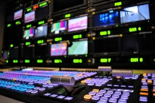 A television control room filled with multiple monitors and keyboards, showcasing a busy broadcasting environment.